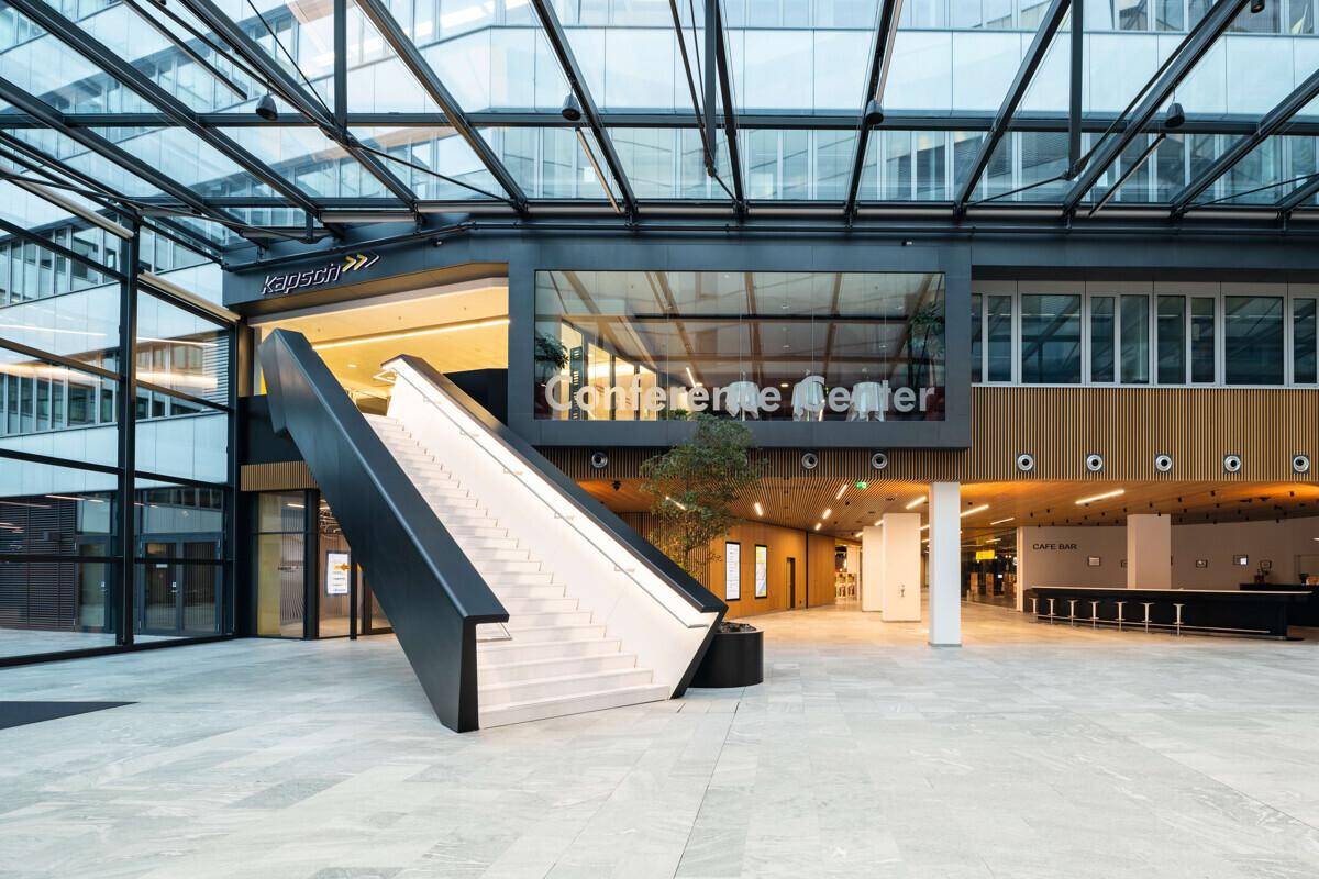 Großzügiges Atrium mit moderner Treppe, Glasdach und Blick auf das Konferenzzentrum, das eine offene Atmosphäre bietet.