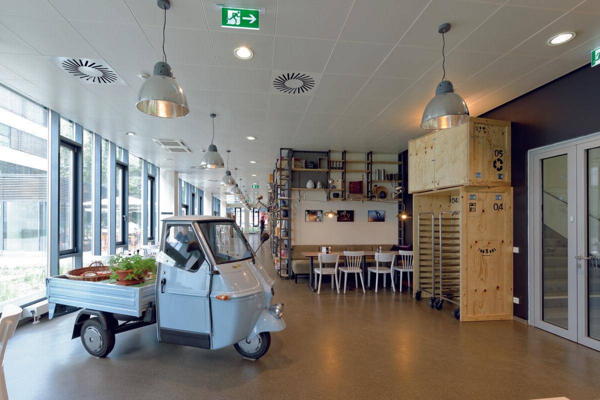 Helle Cafeteria mit großen Fenstern, industriellen Lampen und einem dekorativen Lieferwagen.