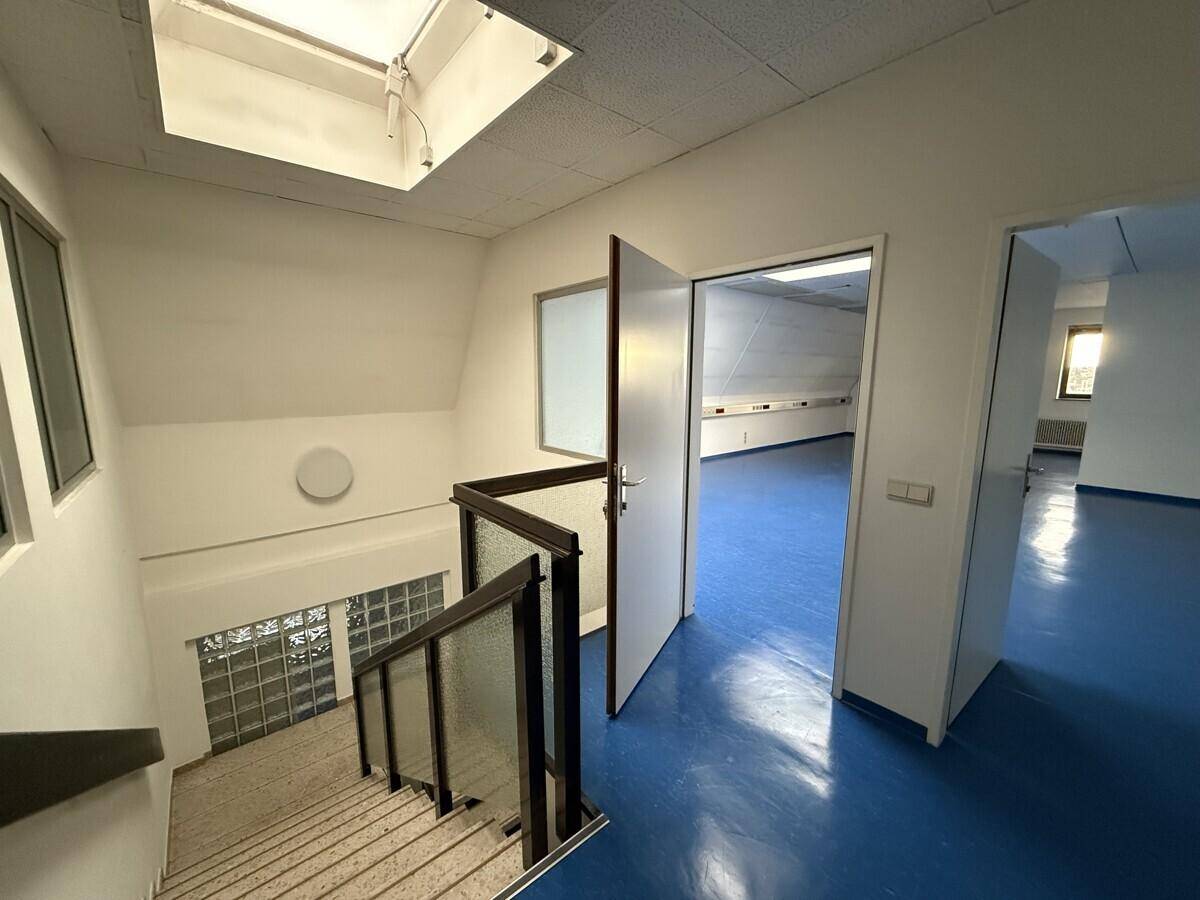 Treppenhaus mit Blick auf eine weitere Etage und einen offenen Bürobereich mit blauen Böden.
