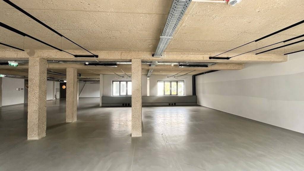 Heller, weitläufiger Gewerberaum mit Betonboden, sichtbaren Installationen und großen Fenstern entlang der Wand.