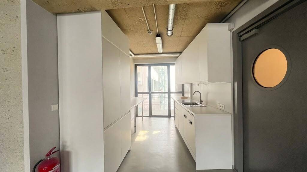 Moderne Küchenzeile mit weißen Schränken und Spüle in einem offenen Gewerbebereich mit viel Tageslicht.