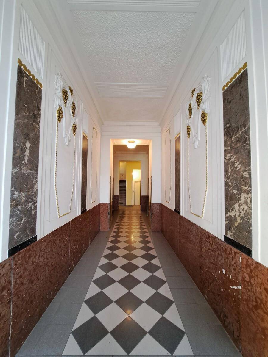 Eleganter Flur mit Schachbrettmuster-Boden, Marmorverkleidung und Stuckverzierungen an den Wänden.