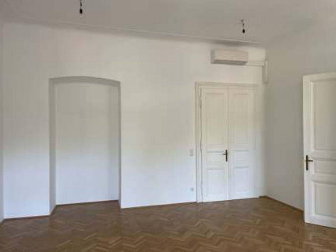 Heller Raum mit Fischgrätparkett, hohen Türen und einer Klimaanlage an der Wand.