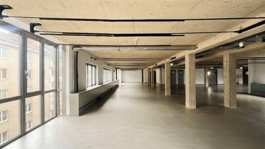 Offener Gewerberaum mit raumhohen Fenstern, die einen Blick auf die umliegenden Stadtgebäude bieten.