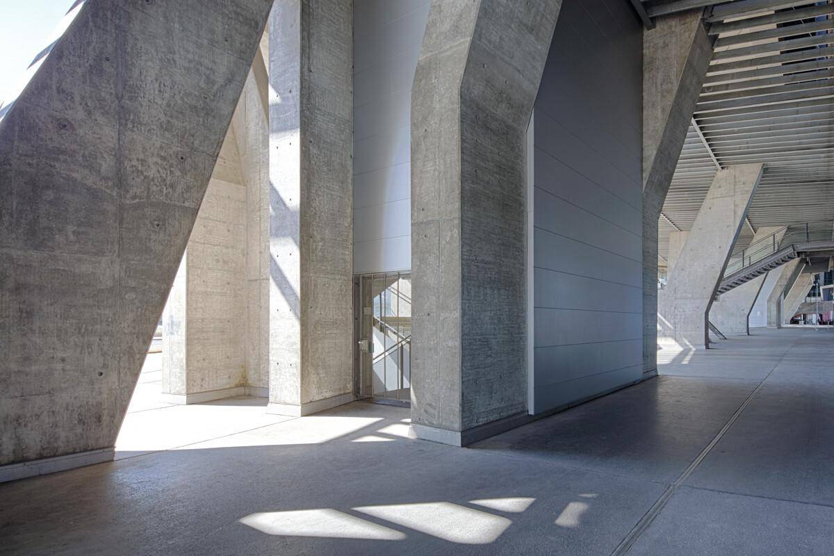 Massive Betonpfeiler stützen eine moderne Gebäudestruktur, mit starkem Lichteinfall und Schatten auf dem Boden.