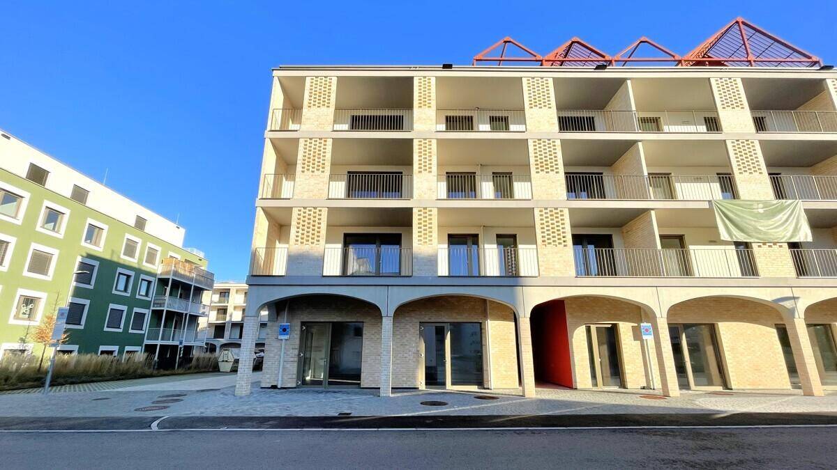 Gesamtansicht eines modernen Mehrfamilienhauses mit Balkonen und Arkaden, umgeben von weiteren Neubauten.