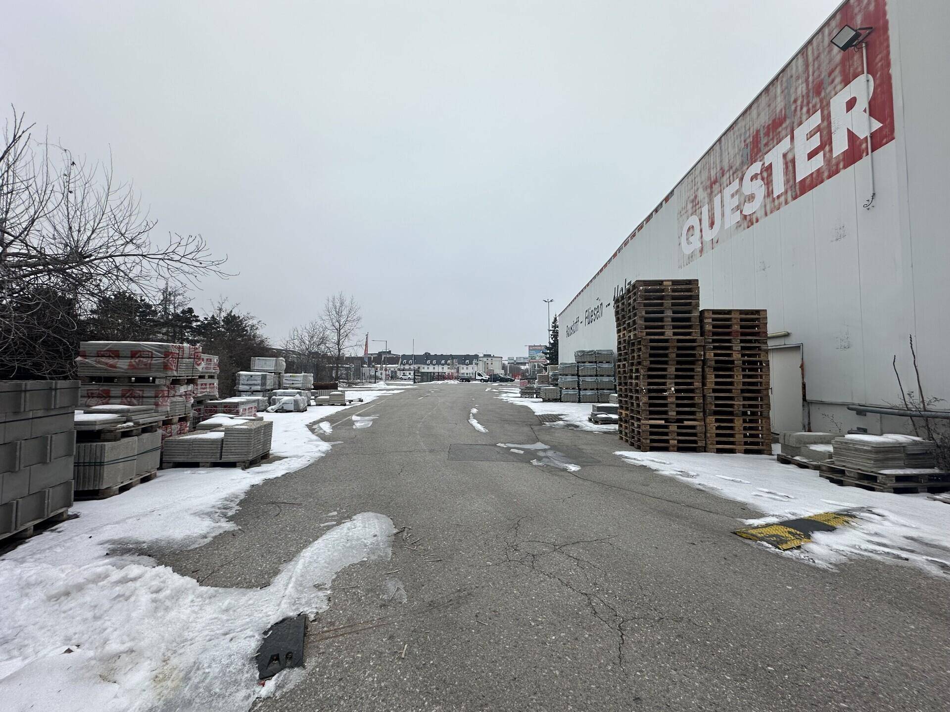 Zufahrtsweg neben dem Gewerbegebäude mit gestapelten Paletten und Baumaterialien am Wegrand.