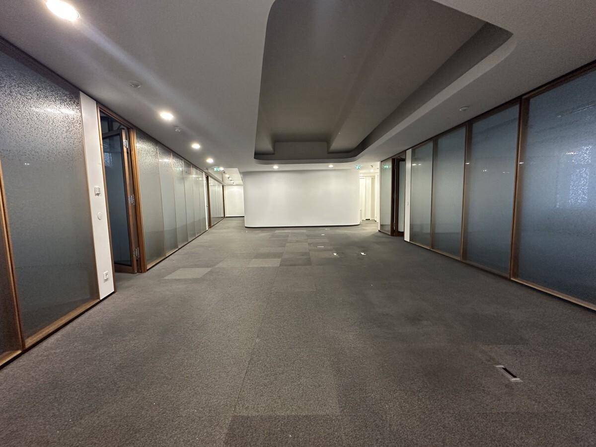 Langer Bürobereich mit Teppichboden und Glaswänden, der verschiedene Arbeitsbereiche abgrenzt und Transparenz bietet.