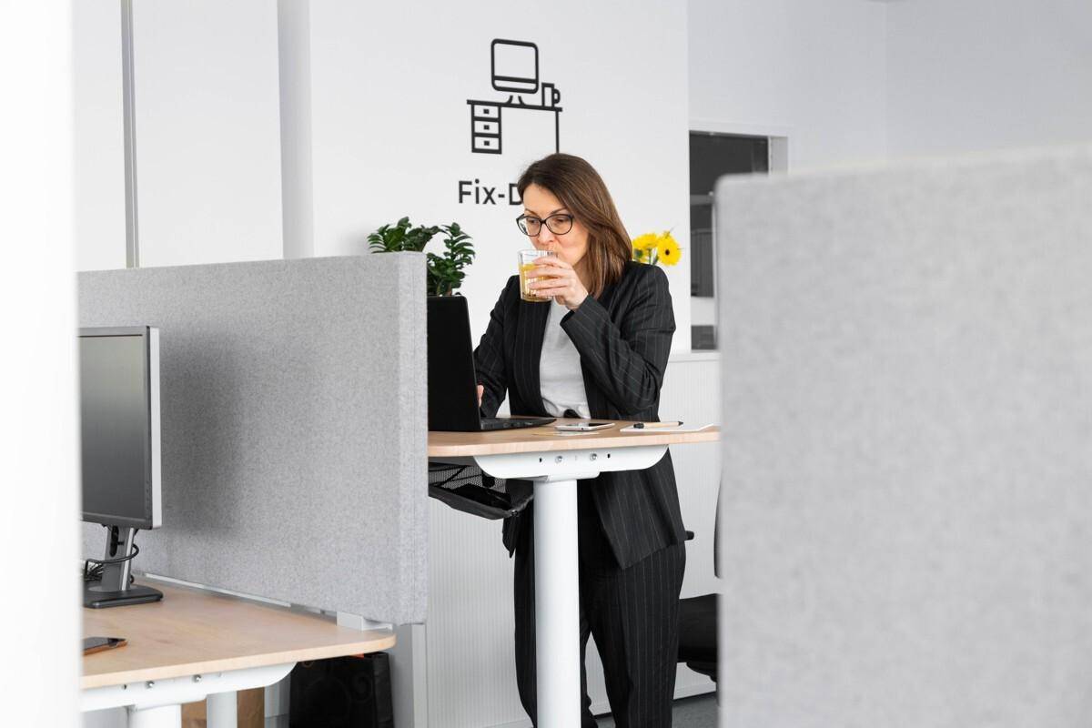 Frau arbeitet an einem höhenverstellbaren Schreibtisch in einem modernen Büro mit Trennwänden und minimalistischem Design.