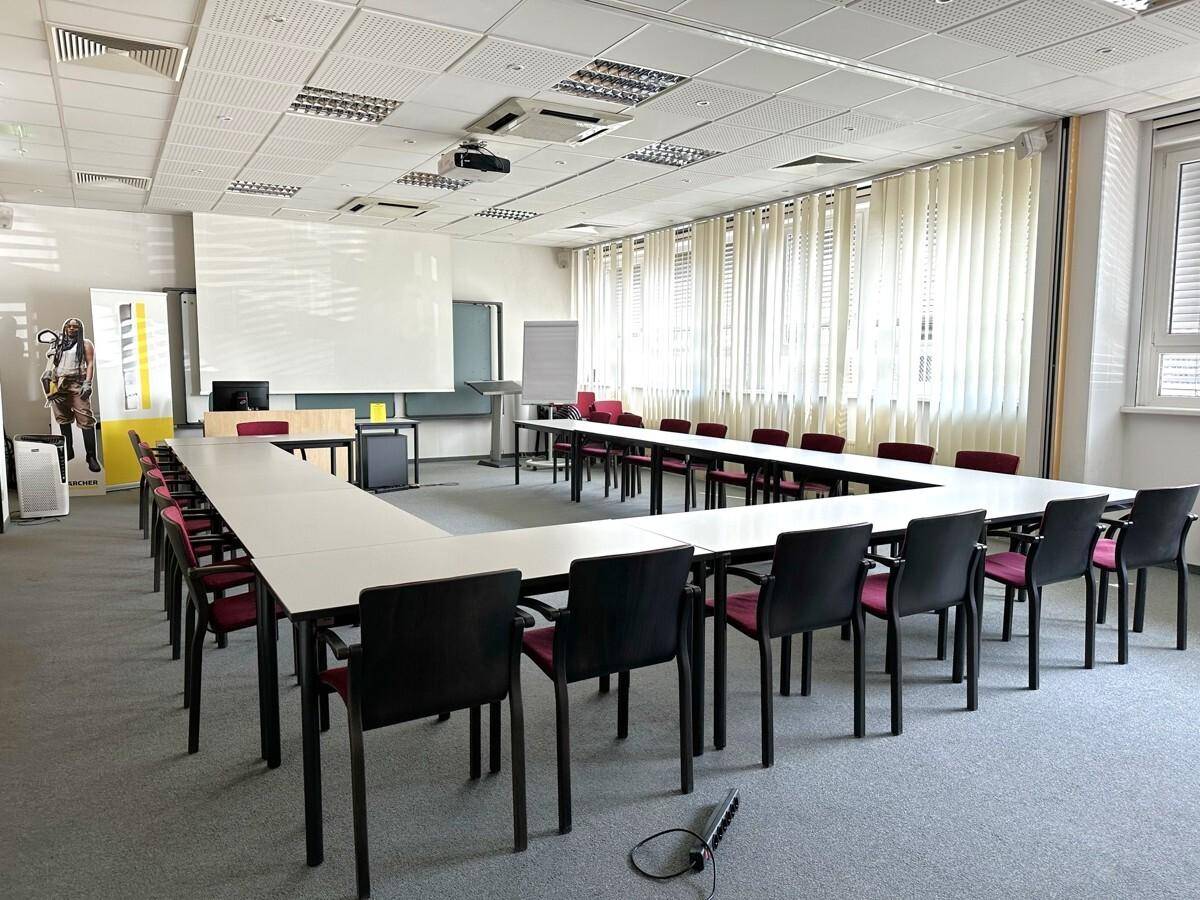 Großer Konferenzraum mit U-förmiger Tischordnung, Projektor und vielen Stühlen für Besprechungen.