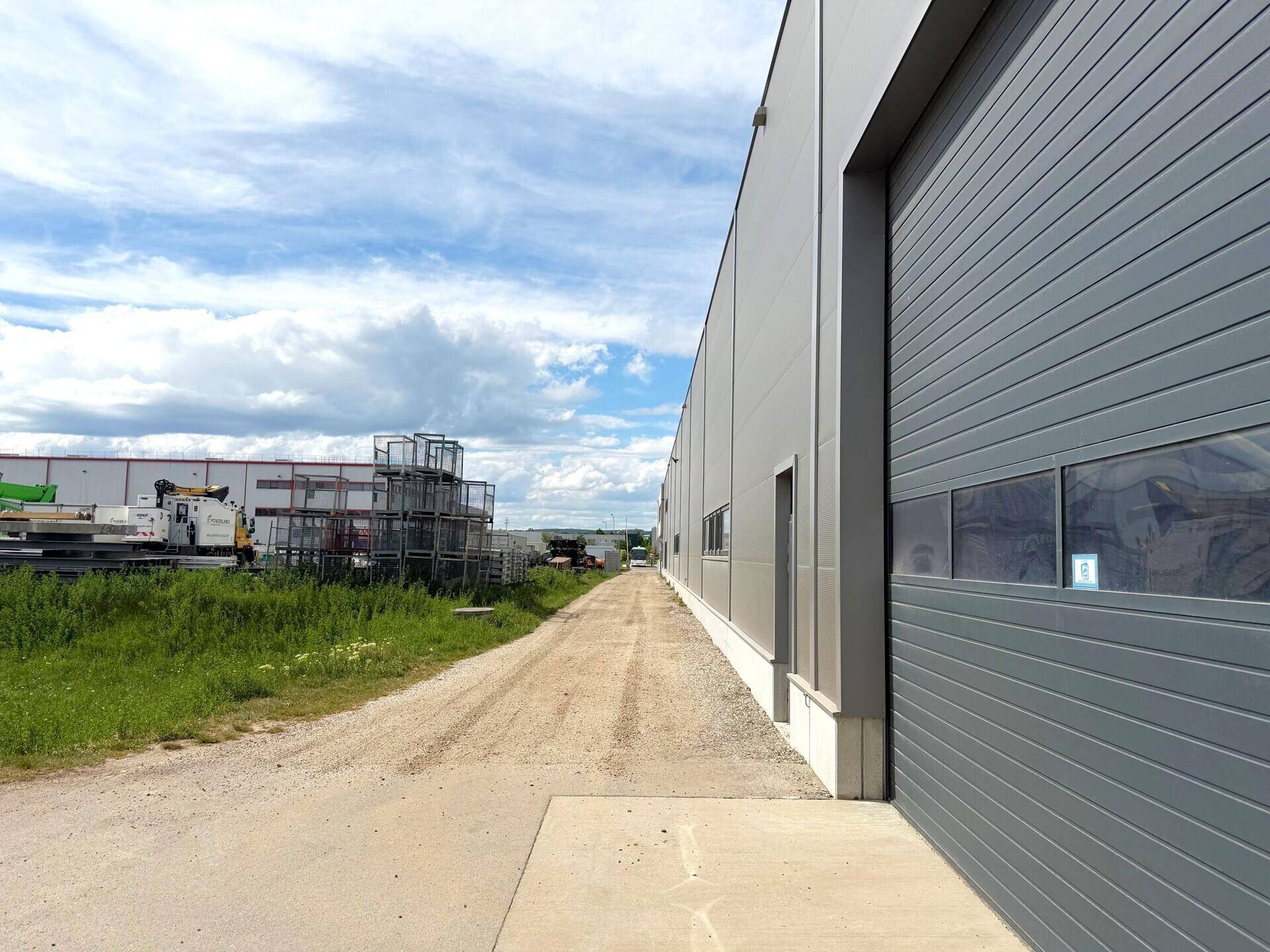 Lange Seitenfassade eines Industriegebäudes mit großem Rolltor und unbefestigter Zufahrt.