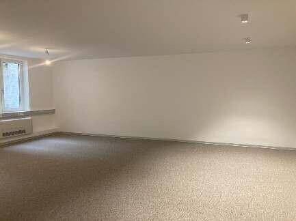 Geräumiger, leerer Büroraum mit hellem Teppichboden und weißen Wänden, bereit zur Einrichtung.