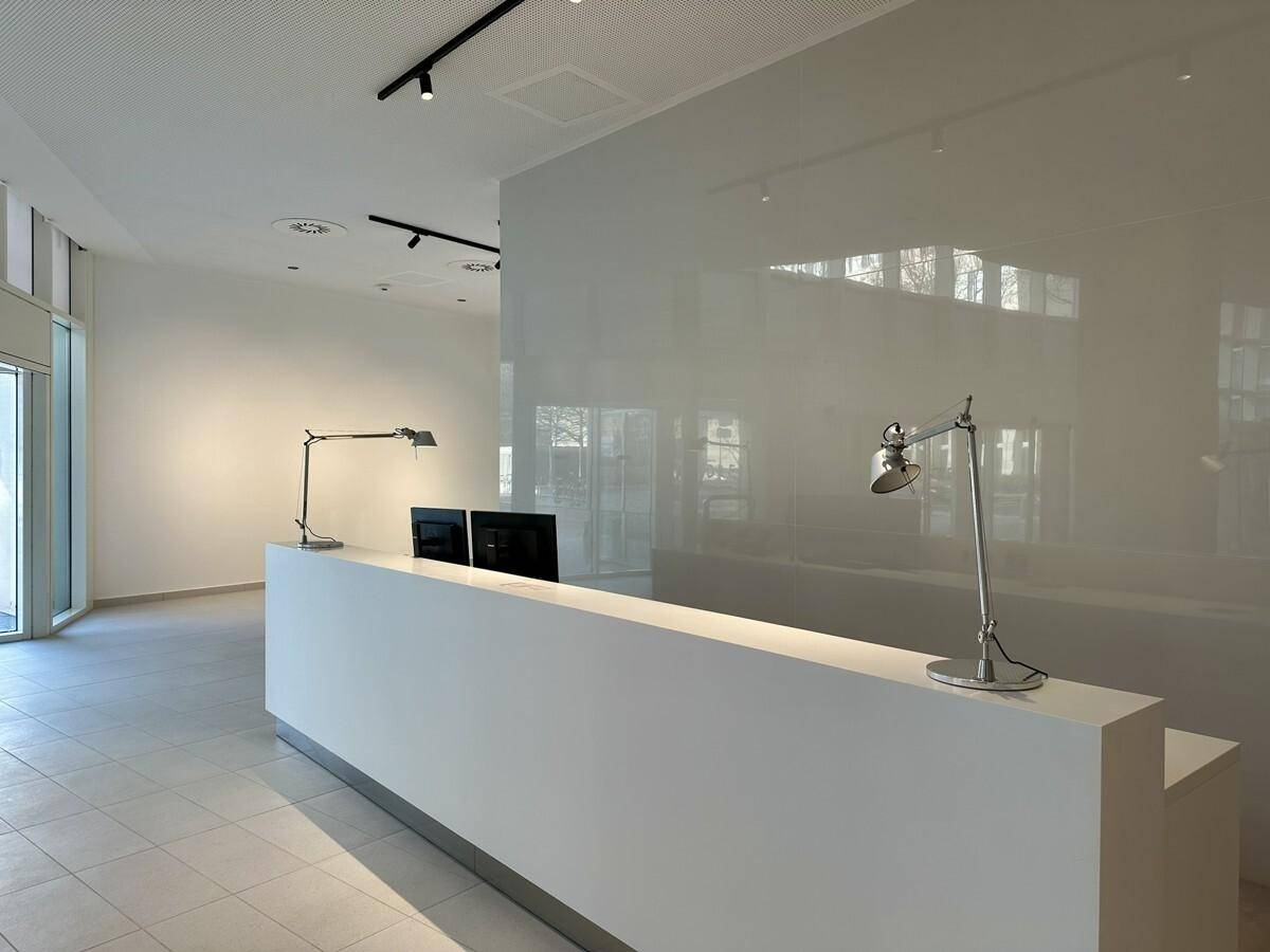 Heller Empfangsbereich mit minimalistischem Schreibtisch, modernen Lampen und glänzender Wand.