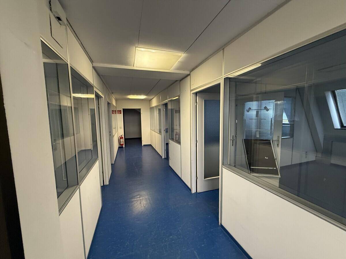 Langer Flur mit blauen Vinylböden und Büros mit Glaswänden auf beiden Seiten.