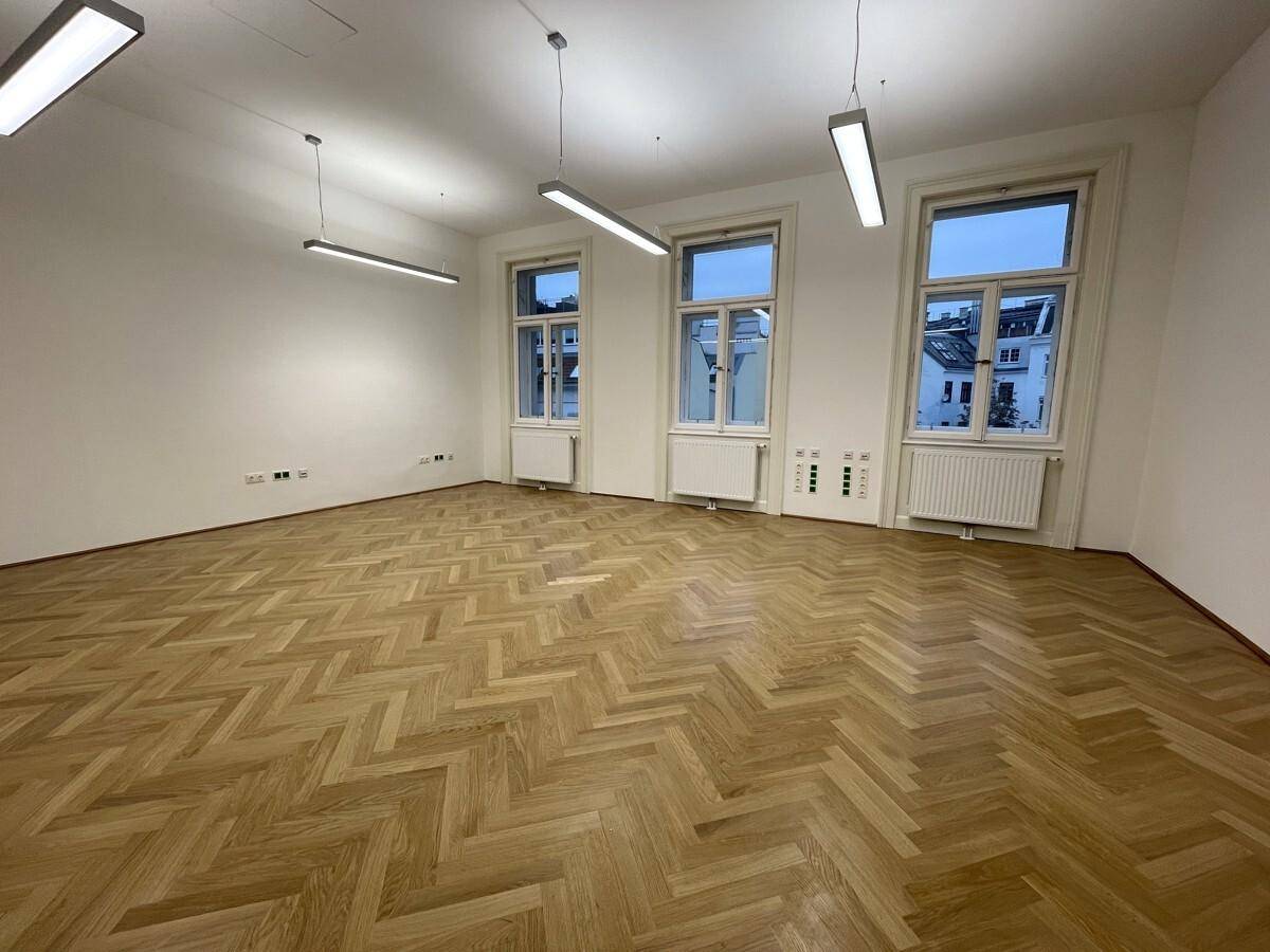 Geräumiger Büroraum mit Fischgrätparkett und drei hohen Fenstern, die eine helle Atmosphäre schaffen.