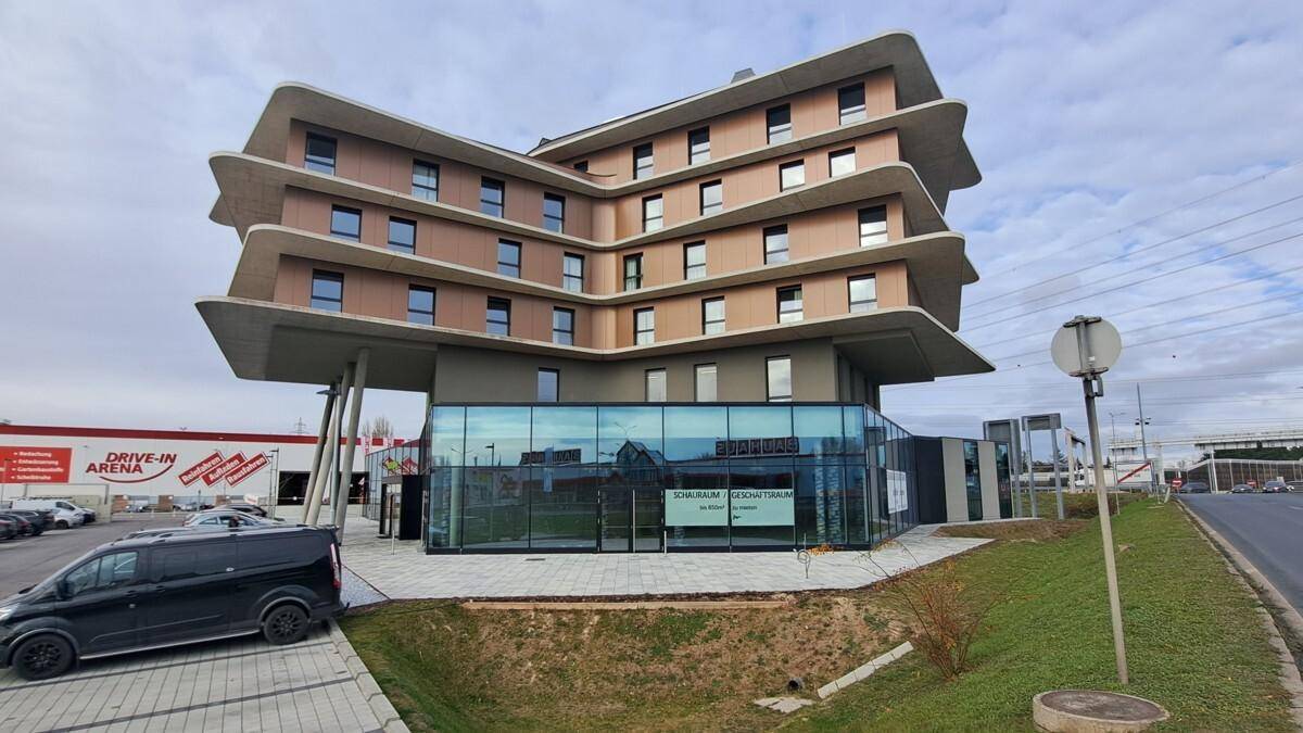 Gesamtansicht des modernen Gebäudes mit Glasfassade und umliegendem Wirtschaftspark, mit einem Lieferwagen im Vordergrund.