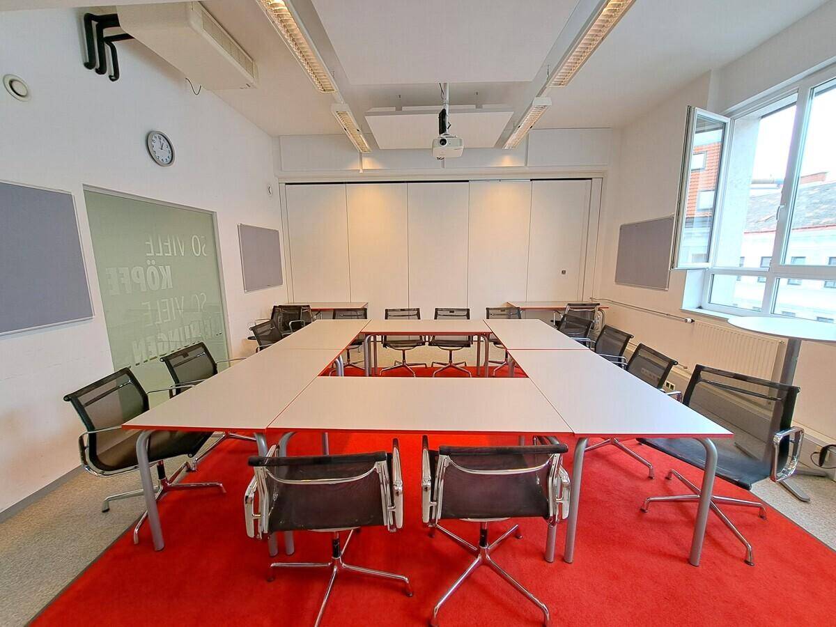 Großer Konferenzraum mit U-förmigem Tisch, vielen Stühlen und einem Projektor für Präsentationen.