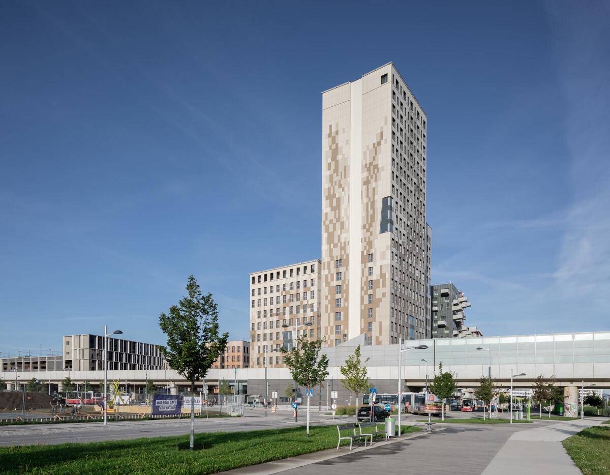 Zeitgenössische Hochhäuser mit auffälliger Fassade entlang einer städtischen Straße mit Bussen und Bäumen.