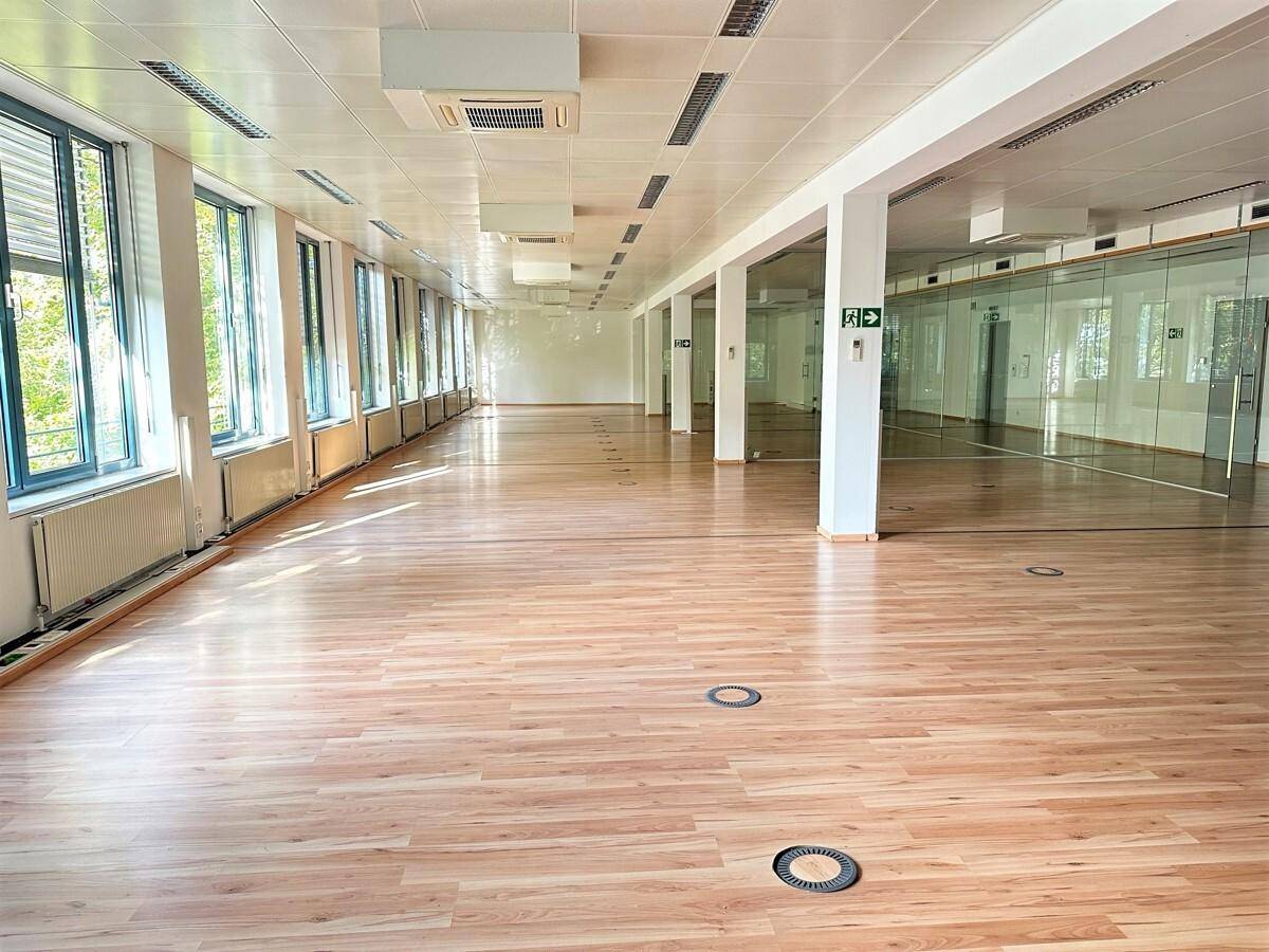 Langer, offener Büroraum mit Holzboden, vielen Fenstern und einer modernen Deckenbeleuchtung.
