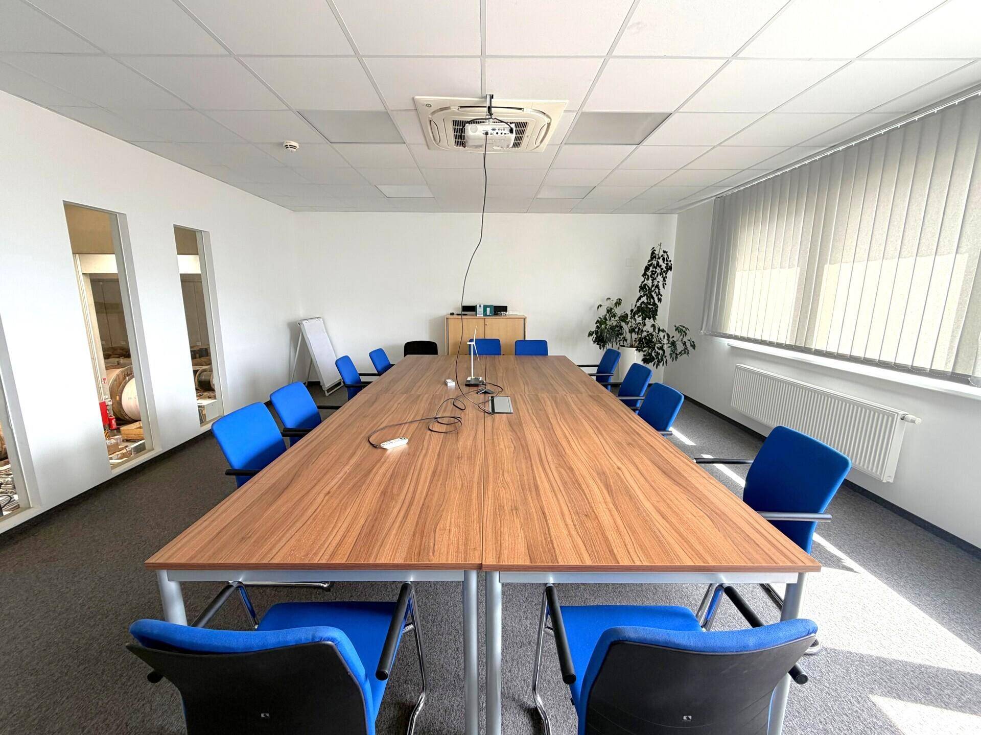 Großer Konferenzraum mit langem Holztisch, blauen Stühlen und Teppichboden.