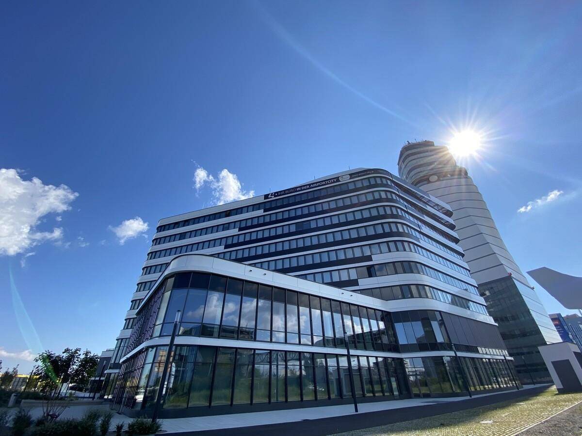 Zeitgenössisches Bürogebäude mit markanter Fassade und Sonnenschein, umgeben von weiterer moderner Architektur.