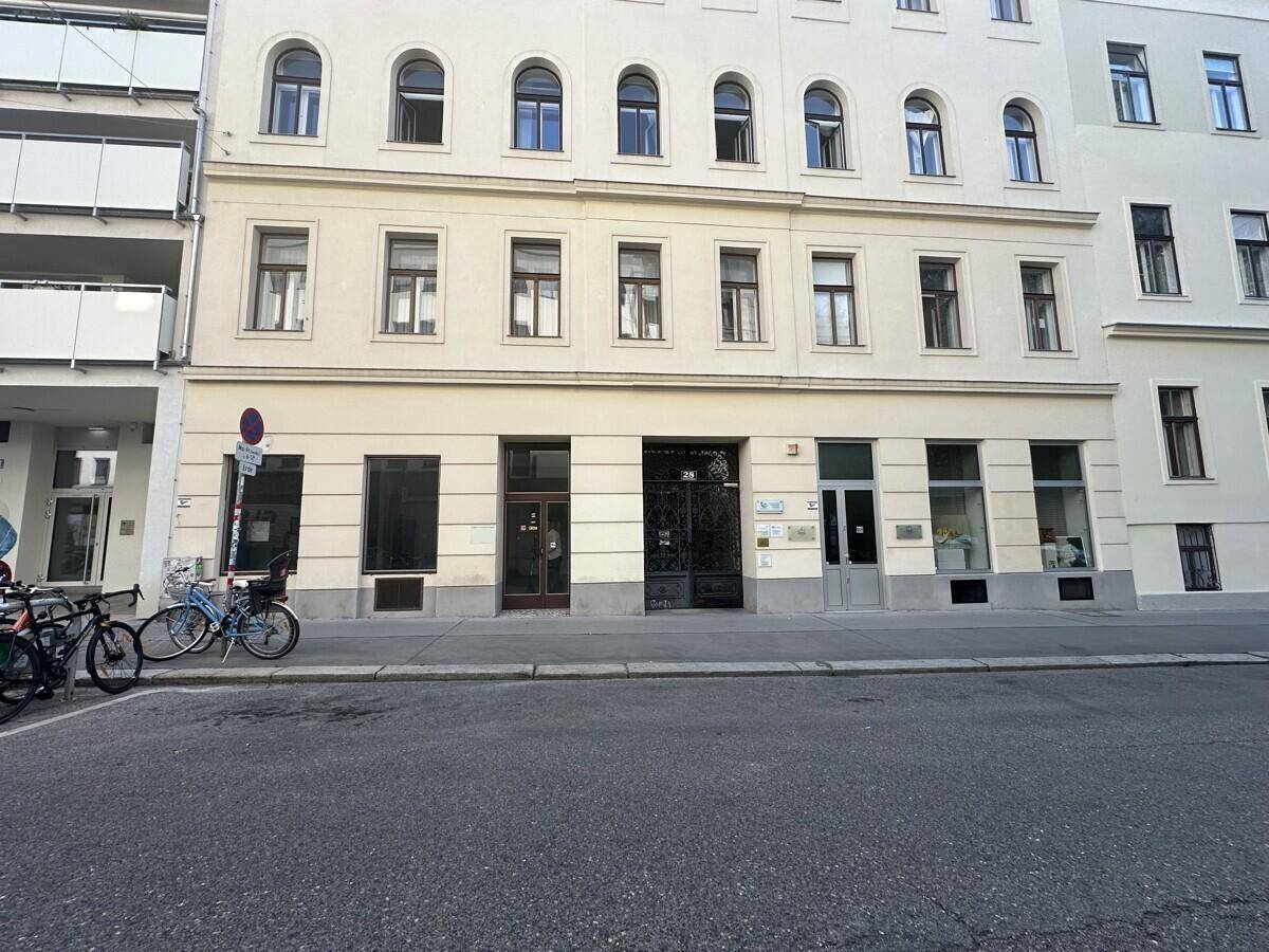 Frontansicht eines Mehrfamilienhauses mit Geschäftsflächen im Erdgeschoss und Wohnungen darüber.
