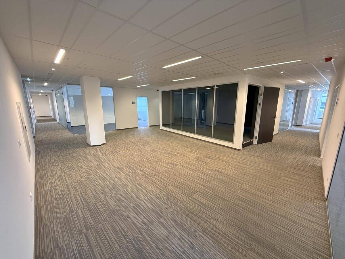 Geräumiger, offener Bürobereich mit Teppichboden und modernen Glasabtrennungen für Arbeitsplätze.