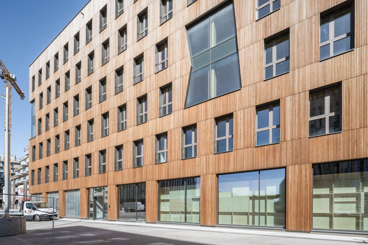 Detailansicht einer modernen Gebäudefassade mit Holzverkleidung und unterschiedlich geformten Fenstern.