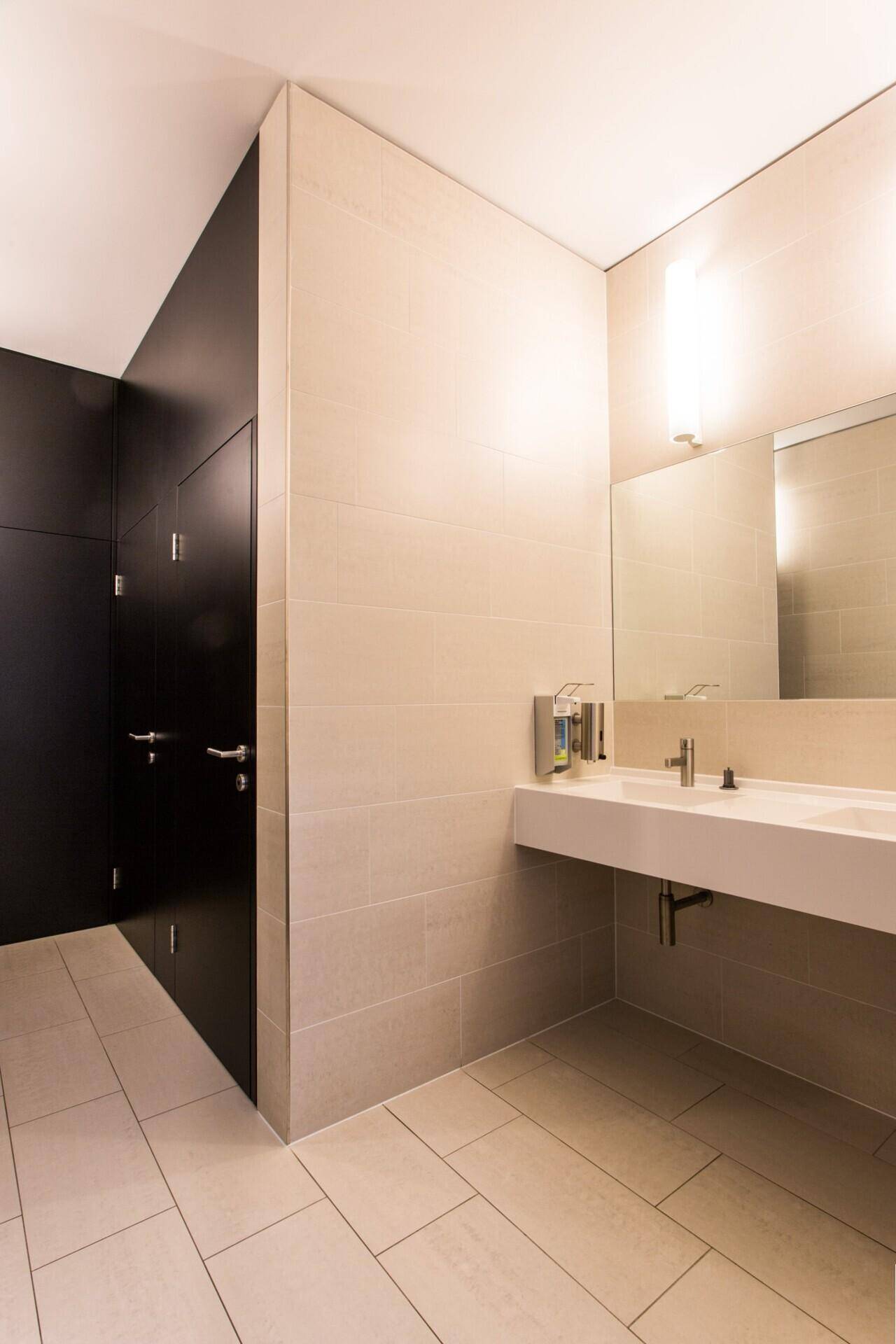 Saubere und moderne Toilettenanlage mit beigefarbenen Fliesen und dunklen Kabinen.