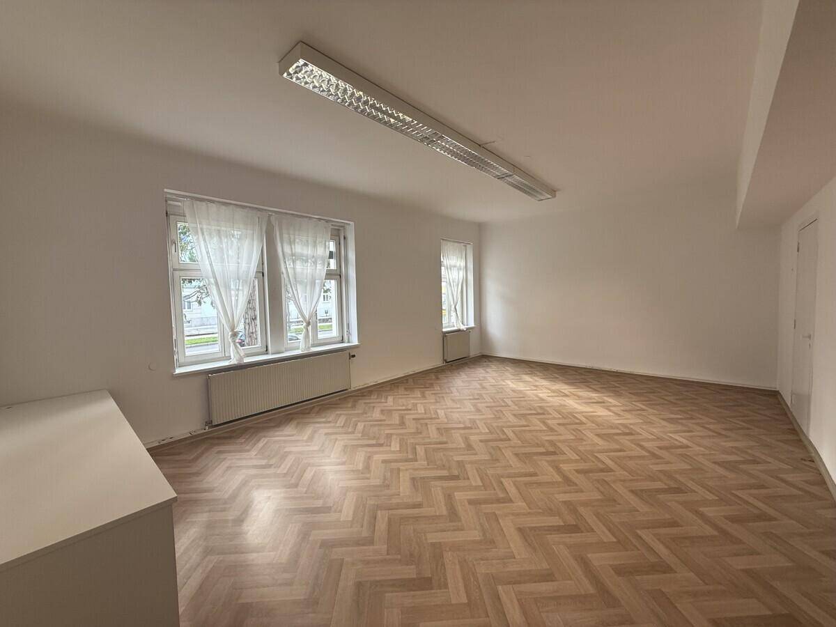 Leerer, heller Raum mit Fischgrätparkett und mehreren Fenstern, vielseitig nutzbar als Büro oder Praxis.