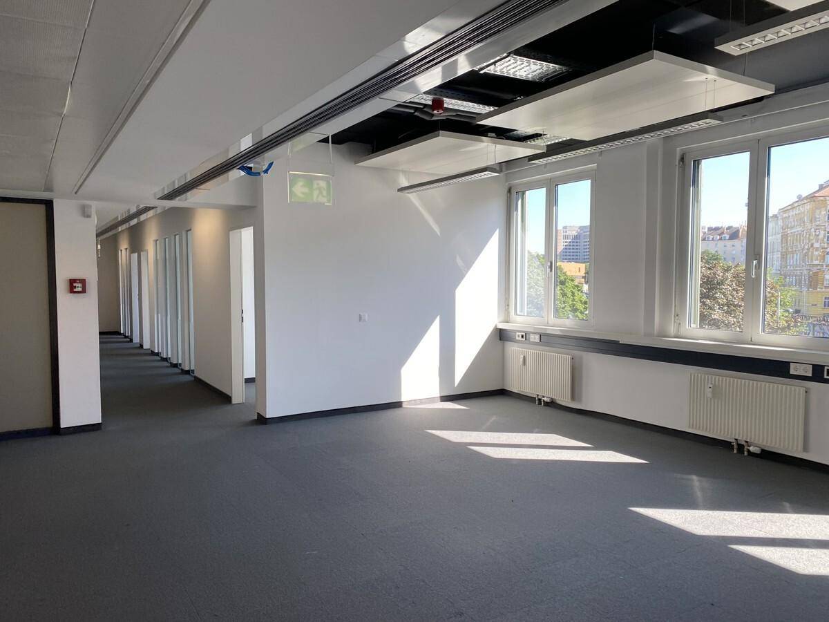 Großes, helles Großraumbüro mit Teppichboden, großen Fenstern und moderner Deckenbeleuchtung.