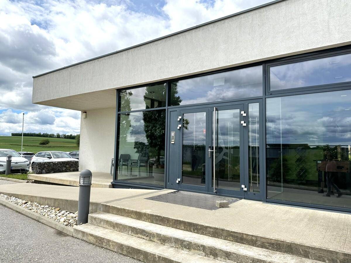 Eingangsbereich eines modernen Gebäudes mit großen Glasfronten und einer breiten Treppe unter bewölktem Himmel.