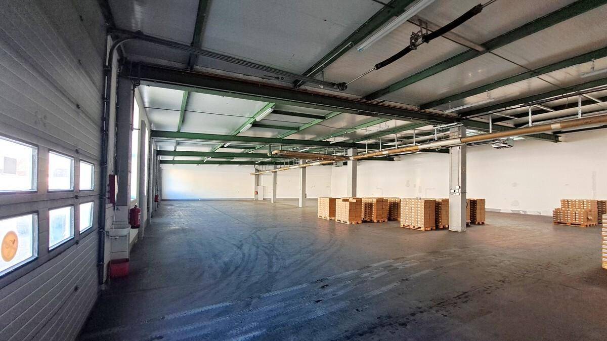 Weitläufige, leere Lagerhalle mit hohen Decken, Betonboden und Tageslicht durch Fenster und Oberlichter.