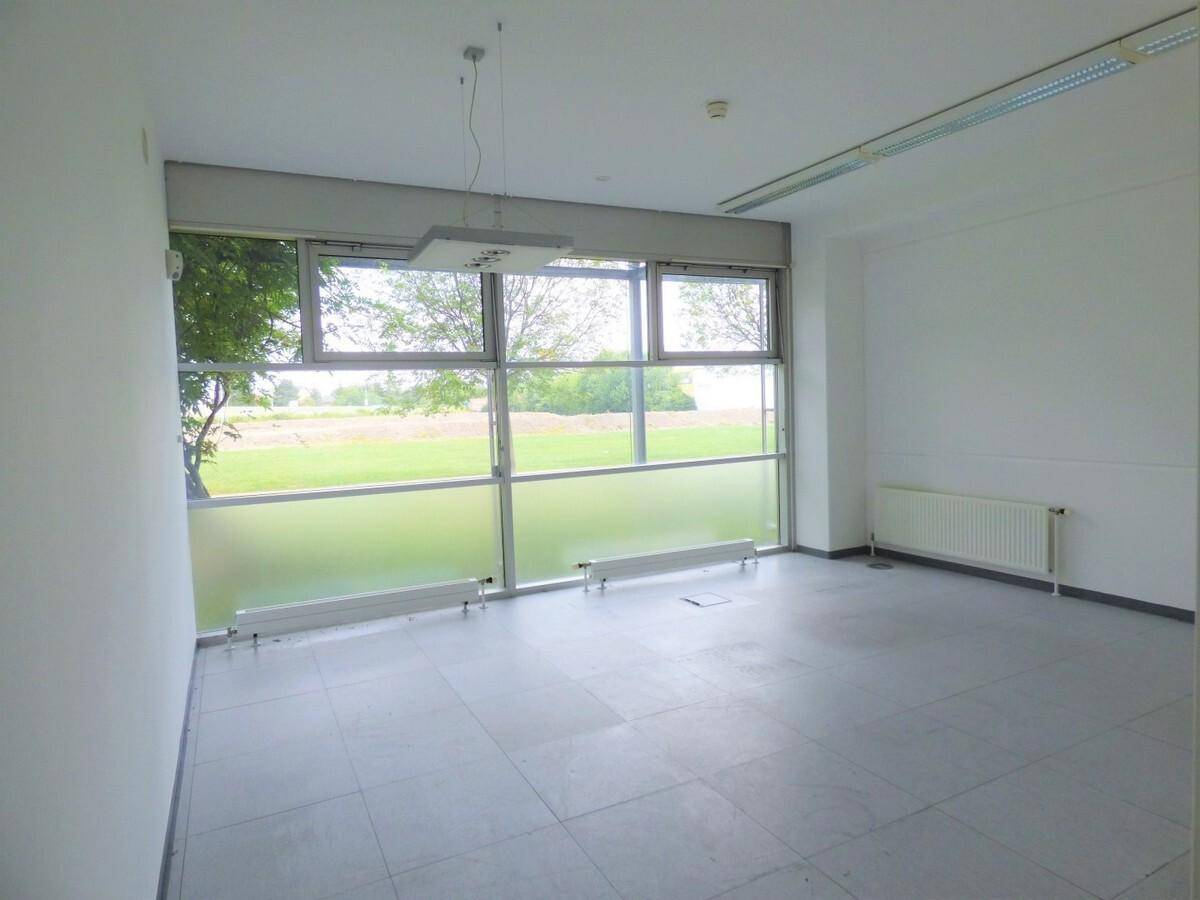 Helles Büro mit Fliesenboden, großen Fenstern und Blick ins Grüne, ausgestattet mit einem Heizkörper.