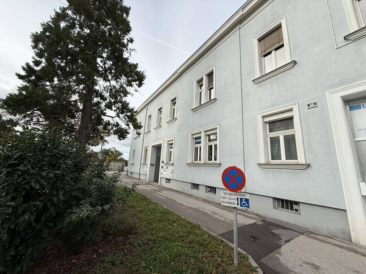Außenansicht eines Gebäudes mit heller Fassade, Fenstern und einer barrierefreien Rampe am Eingang.