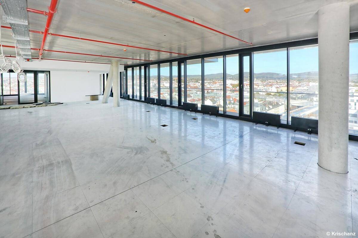 Großer, offener Büroraum im Rohbau mit hohen Decken und weitem Stadtblick durch die Fenster.