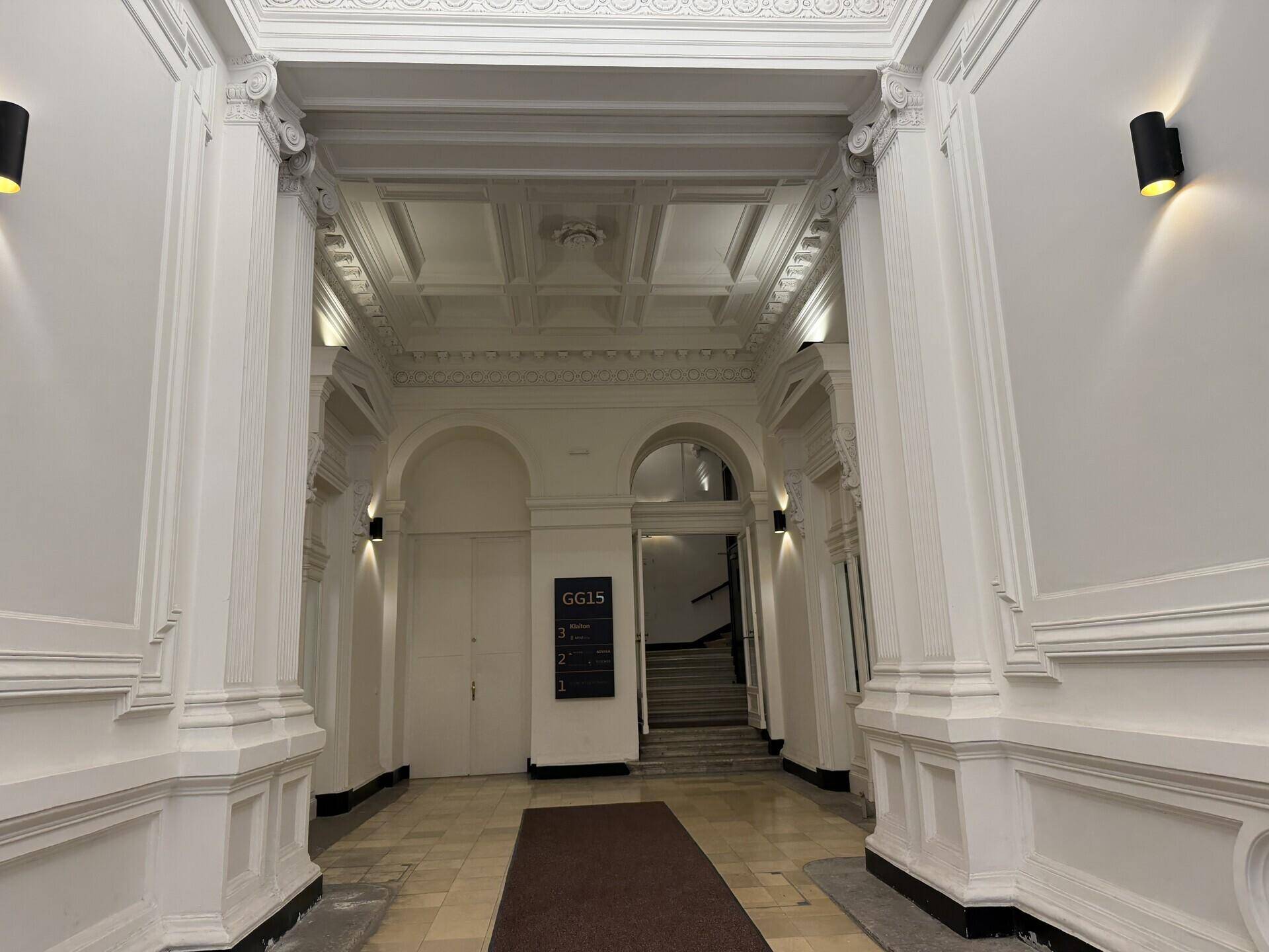 Eleganter Eingangsbereich mit hohen Säulen, Stuckdecken und klassischer Architektur in Weißtönen.