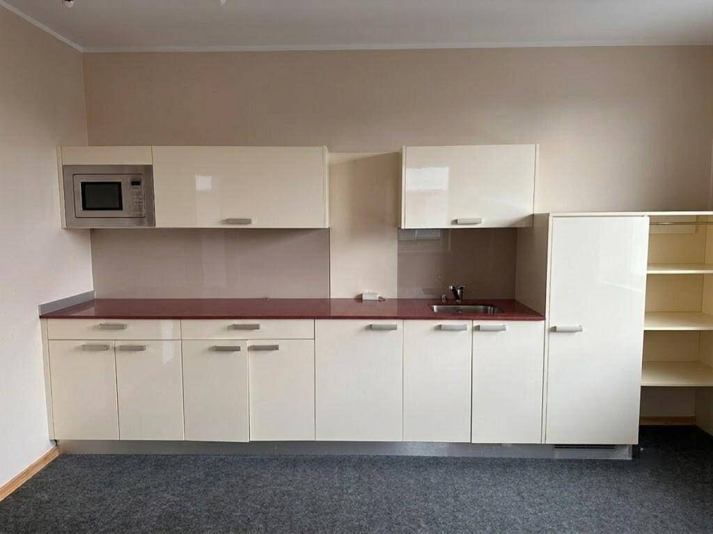 Kleine Küchenzeile mit glänzenden beigen Schränken, roter Arbeitsplatte und integrierter Mikrowelle.