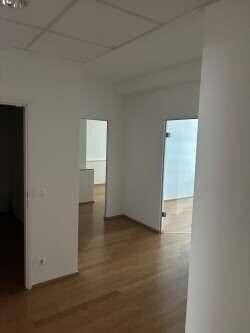 Ein heller Flur mit Holzboden, weißen Wänden und mehreren Türen, die zu Büroräumen führen.