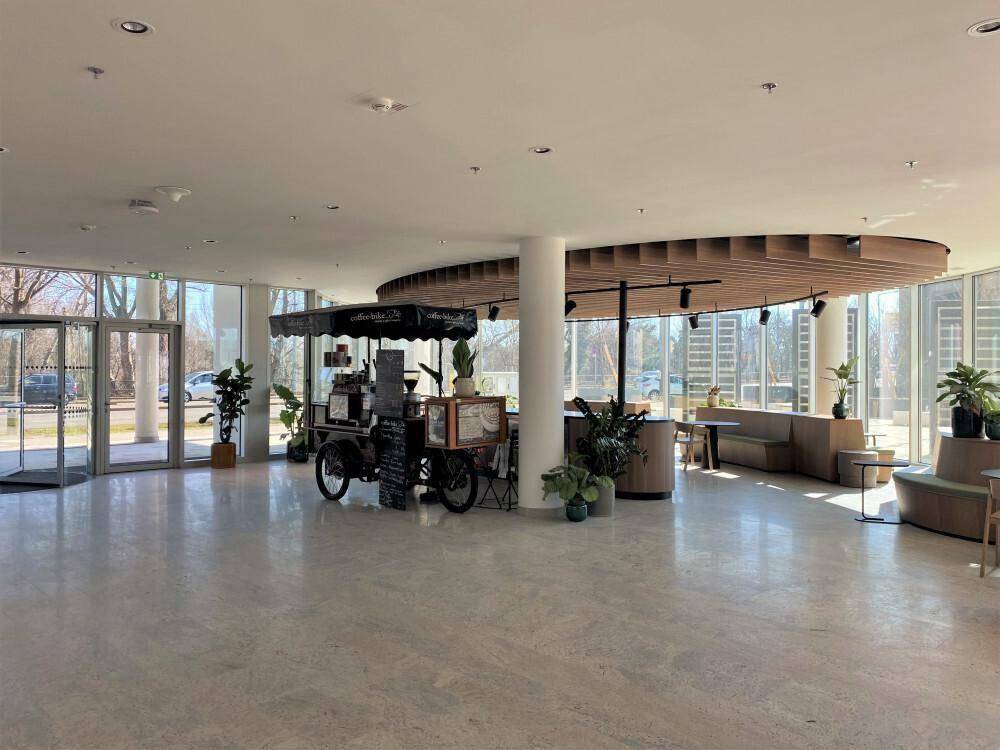 Geräumige und helle Lobby mit einem mobilen Kaffeestand, Holzelementen und großen Fensterfronten.