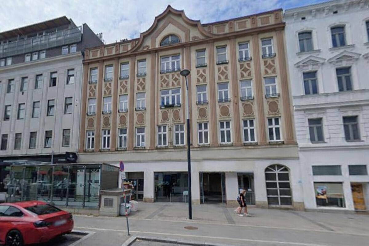 Breitere Straßenansicht des historischen Gebäudes mit angrenzenden Häusern und parkenden Autos.