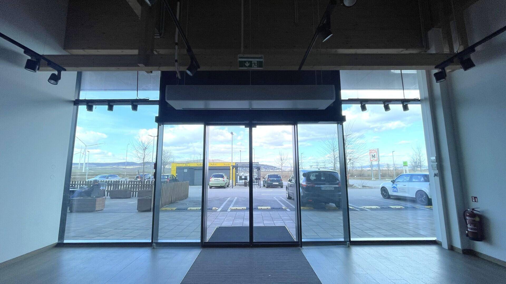 Innenansicht des Eingangsbereichs mit großen Glasfenstern, automatischen Türen und Blick auf den Parkplatz.