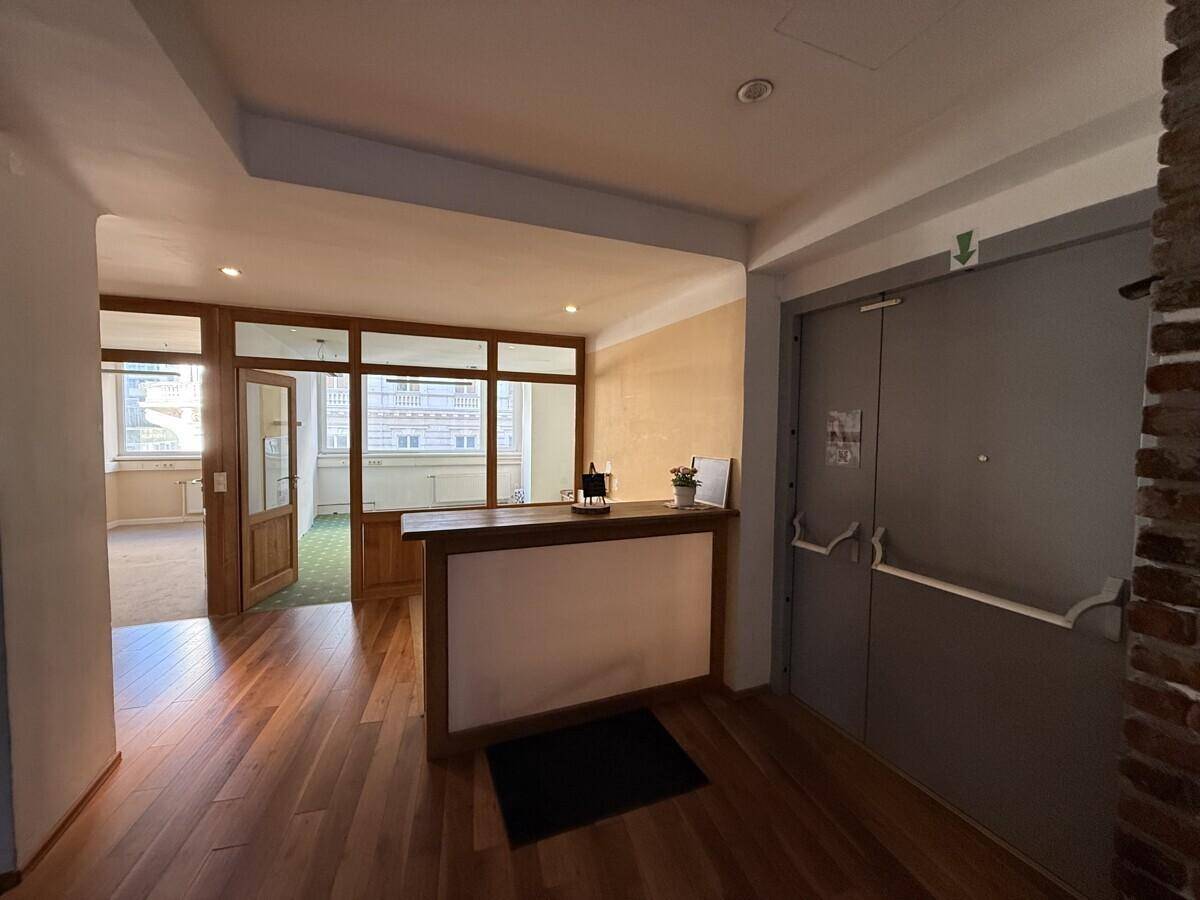 Empfangsbereich mit Holzboden, einer Rezeptionstheke und Zugang zu weiteren Räumen durch Glastüren.