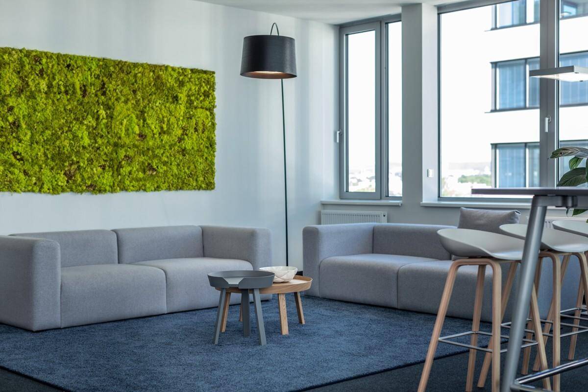 Stilvoller Loungebereich mit bequemen Sofas, Stehlampe und einer auffälligen Mooswand.