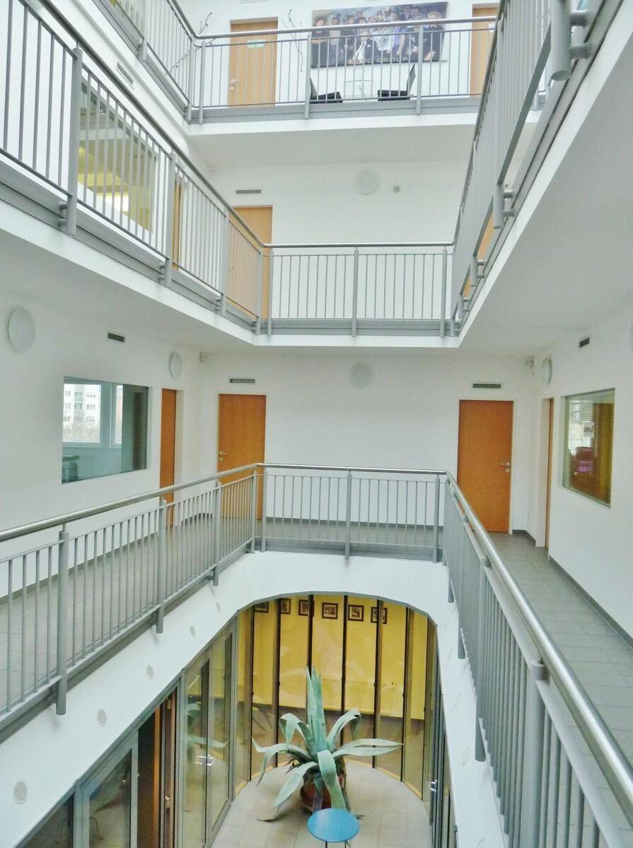 Heller, mehrstöckiger Innenhof mit offenen Gängen, Metallgeländern und einer großen Pflanze im Zentrum.