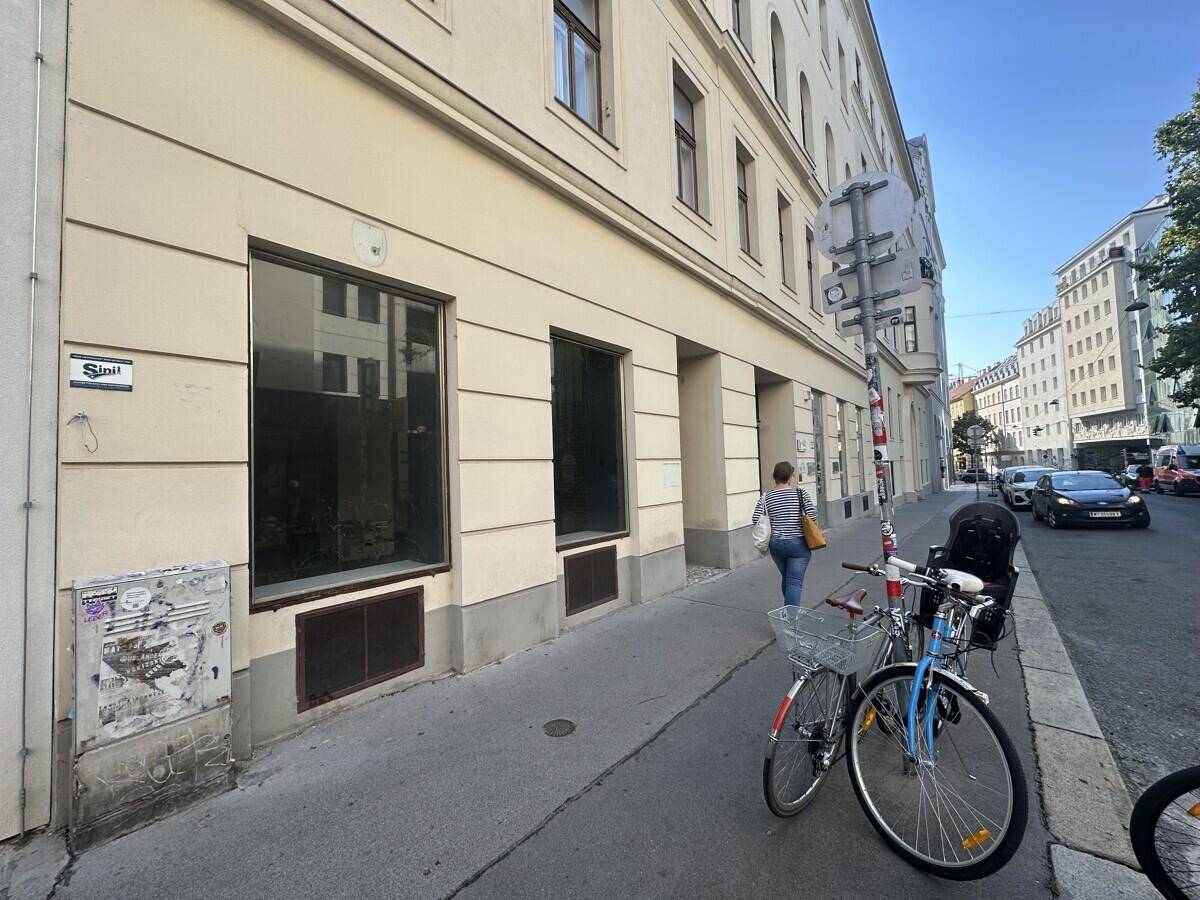 Seitenansicht eines Geschäftsgebäudes an einer belebten Straße mit Fahrrädern und Passanten.