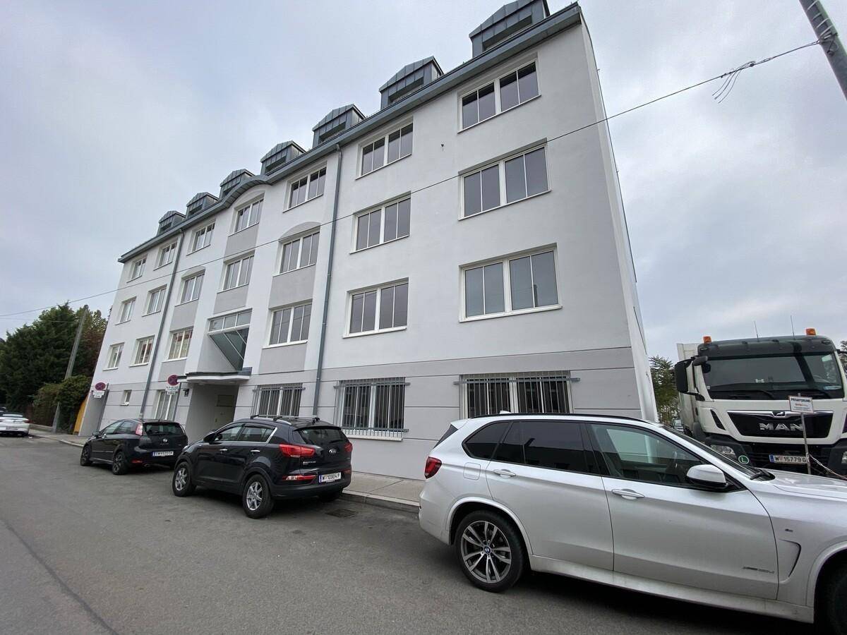 Mehrstöckiges Wohngebäude mit weißer Fassade und vielen Fenstern, umgeben von parkenden Autos.