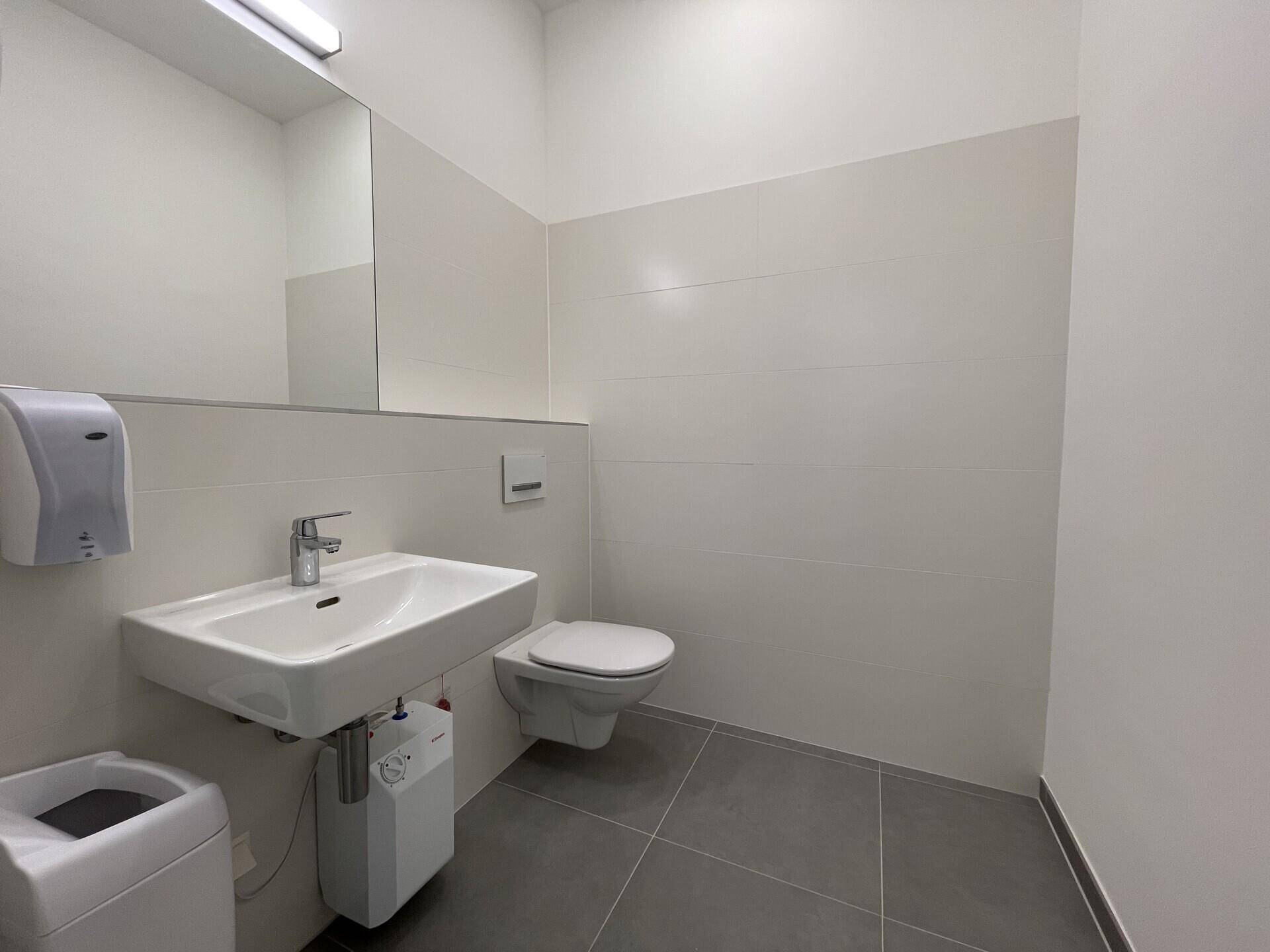 Modernes Badezimmer mit weißen Wandfliesen, grauen Bodenfliesen, wandhängendem WC und Waschbecken.