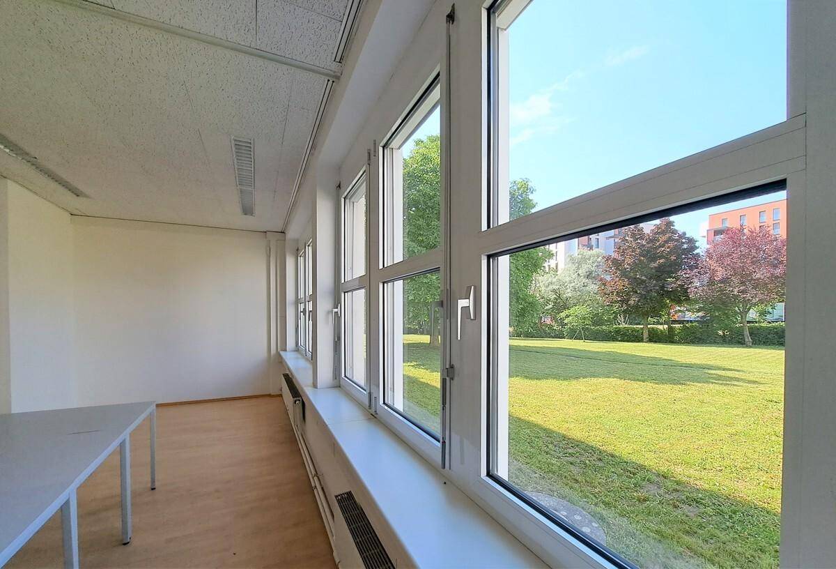 Helles Büro mit großen Fenstern und Blick ins Grüne, ausgestattet mit einem einfachen Tisch.