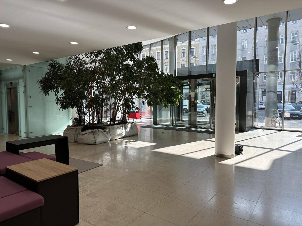 Geräumige Lobby mit großen Fenstern, viel Tageslicht, Pflanzen und Sitzgelegenheiten für Besucher.